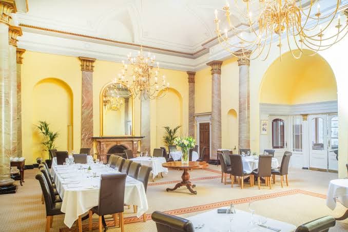 The dining room at Clifton Members Club: chandeliers, marble columns and a long set table